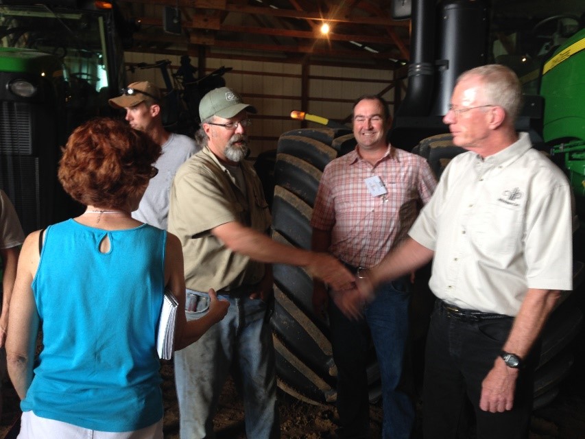 Two men shaking hands next to tractors