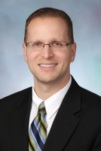Headshot of a man wearing glasses and a striped tie