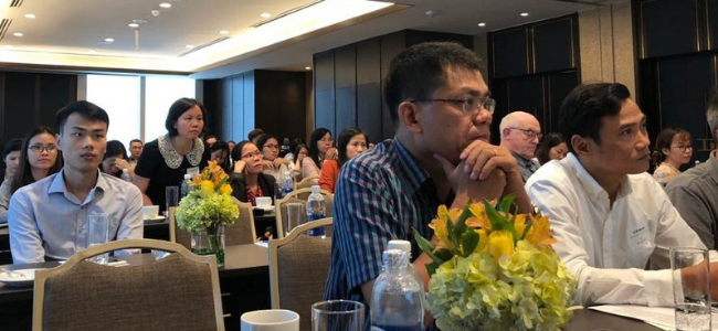 image of people sitting at tables in a conference room listening to a speaker