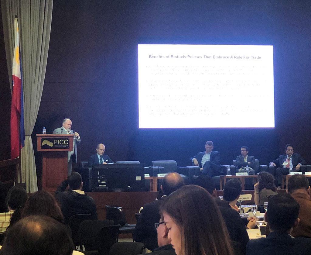 Speaker at Bioenergy Week- speaking on stage behind a podium with 4 panelist sitting on stage