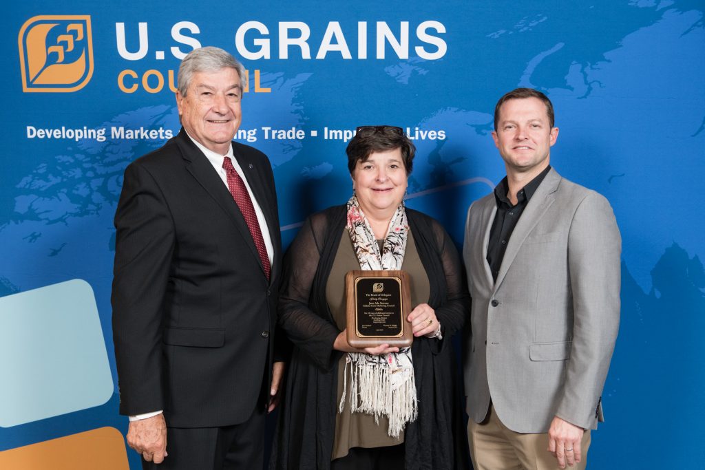 Jane Ade Stevens Recognition- 2 men & 1 woman standing in front of the USGBC banner, woman in the middle holding recognition plaque