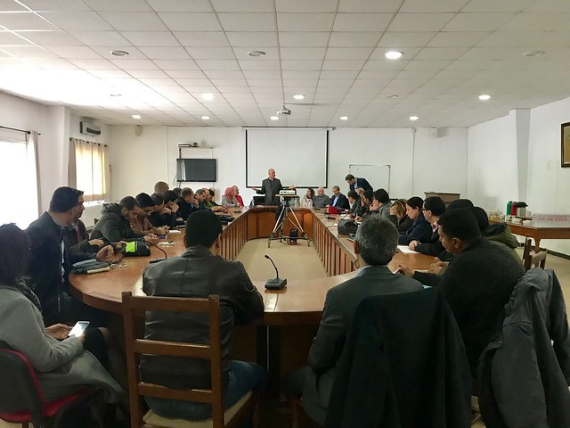 Tunisia DDGS- attendees seated in a meeting at a large table in the shape of an oval listening to a man present