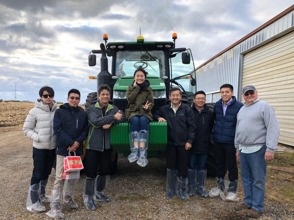 Taiwan DDGS Team- 8 team members standing infront of a green tractor, one team member sitting on the tractor