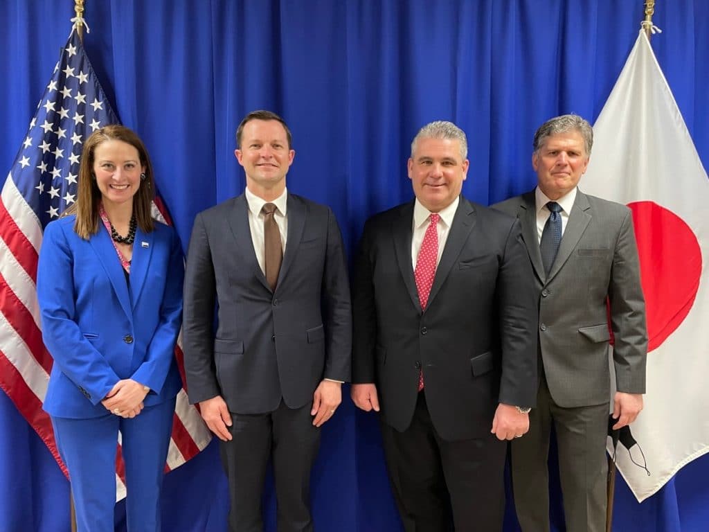 1 woman and 3 men standing in front of a US and Japan flag