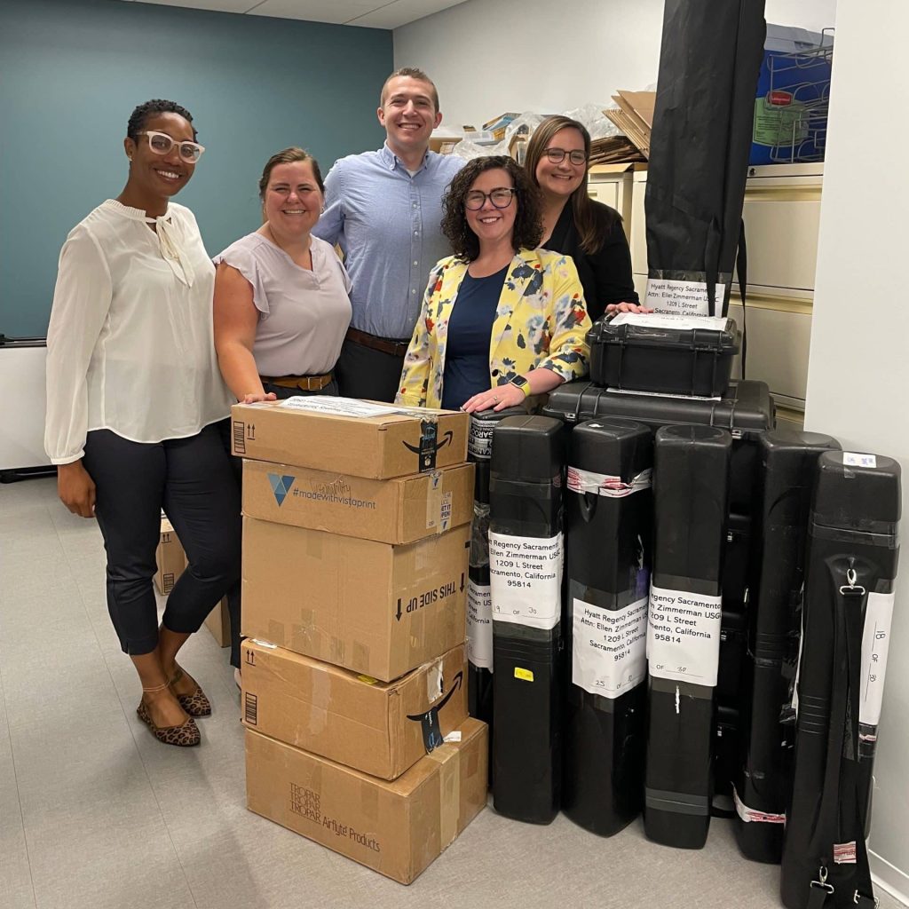 image of four women and a man smiling with a stack of boxes