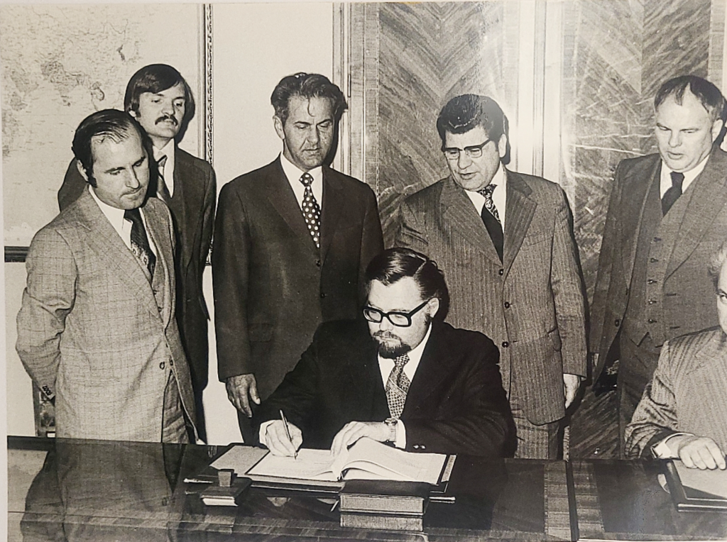 image of men watching another man sign a protocol
